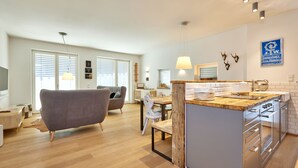 Una cocina moderna con una isla de madera, armarios blancos y un área de comedor con sofá gris y mesa de madera.