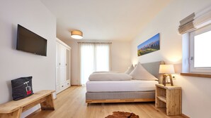 Un dormitorio con cama, un banco de madera, televisor montado, lámpara, pintura y alfombra de piel.