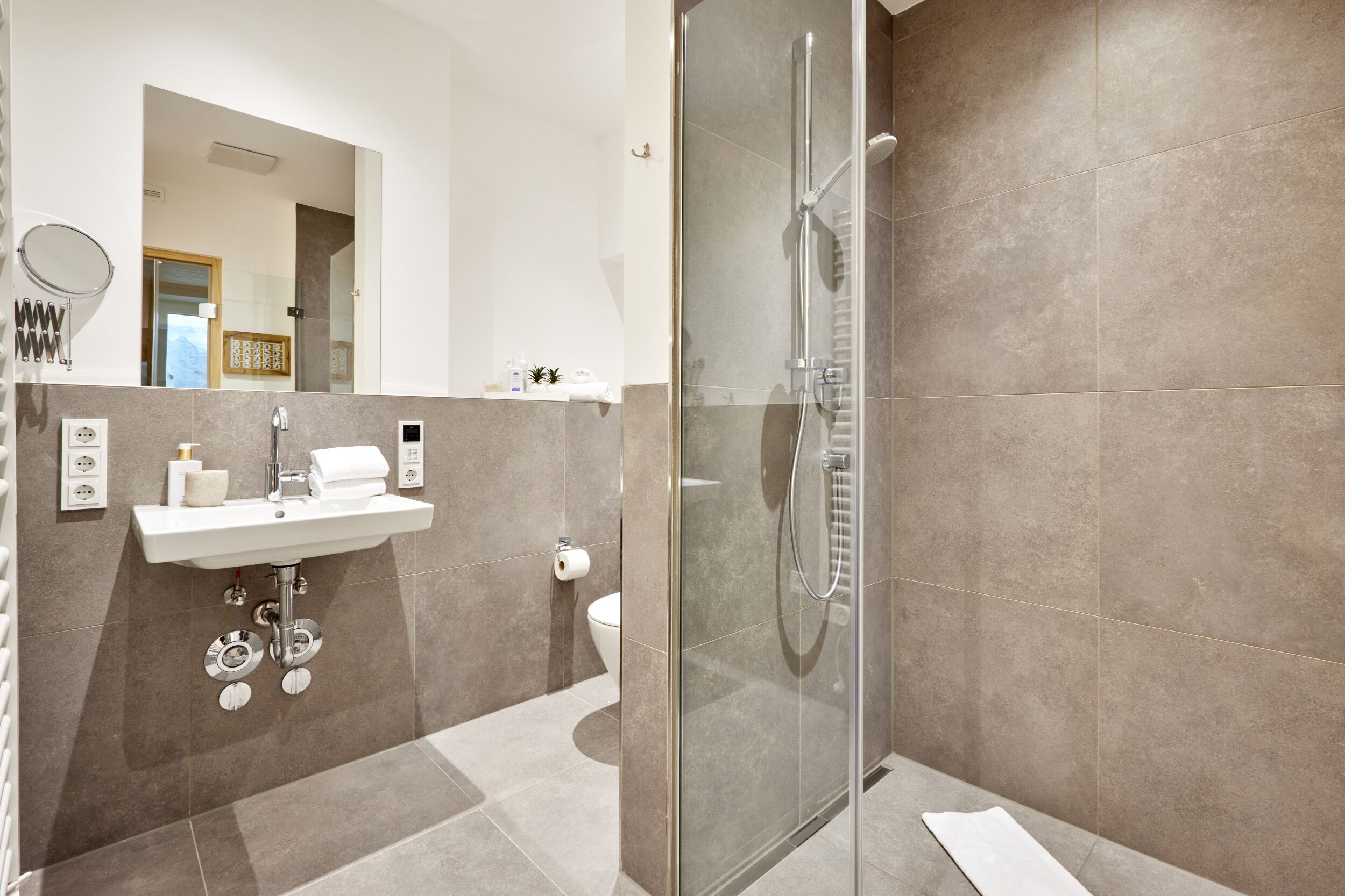 Een moderne badkamer met een douche met glazen wand, een wastafel met spiegel en een toilet.