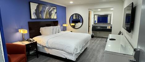 Habitación de hotel con cama, mesita de noche, lámpara y baño con lavabo y espejo.