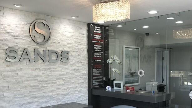 A reception area with a stone wall, a large S logo, and a sign detailing checkout times and policies. - Sands Motel (Riverside)