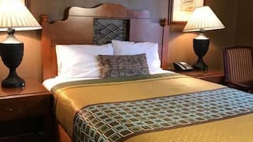 A hotel room with a large bed, two bedside tables, a nightstand, a headboard with a decorative panel, and two wall-mounted lamps.