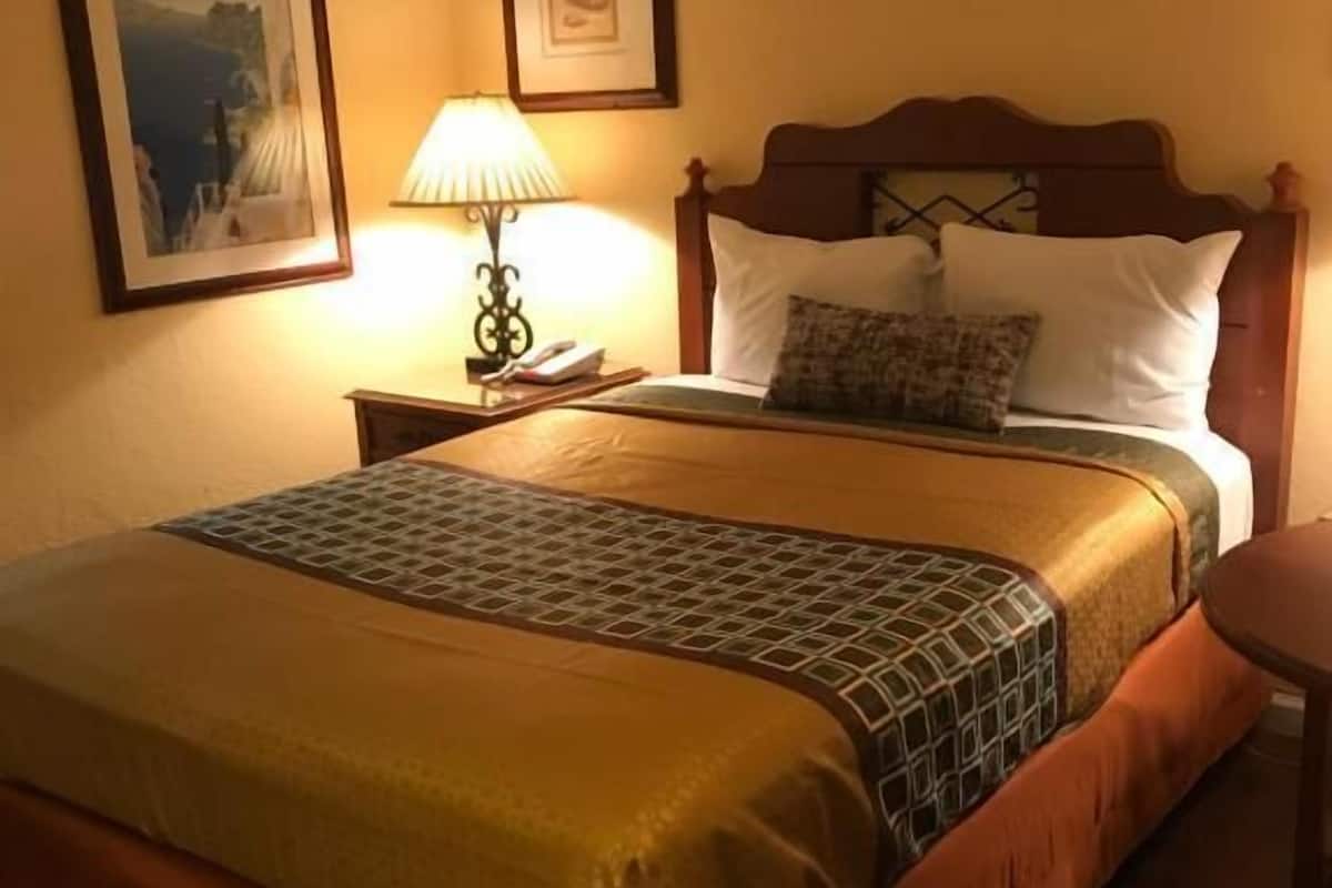 Ein Hotelzimmer mit einem großen Bett, einem Nachttisch mit Lampe und zwei gerahmten Bildern an der Wand.