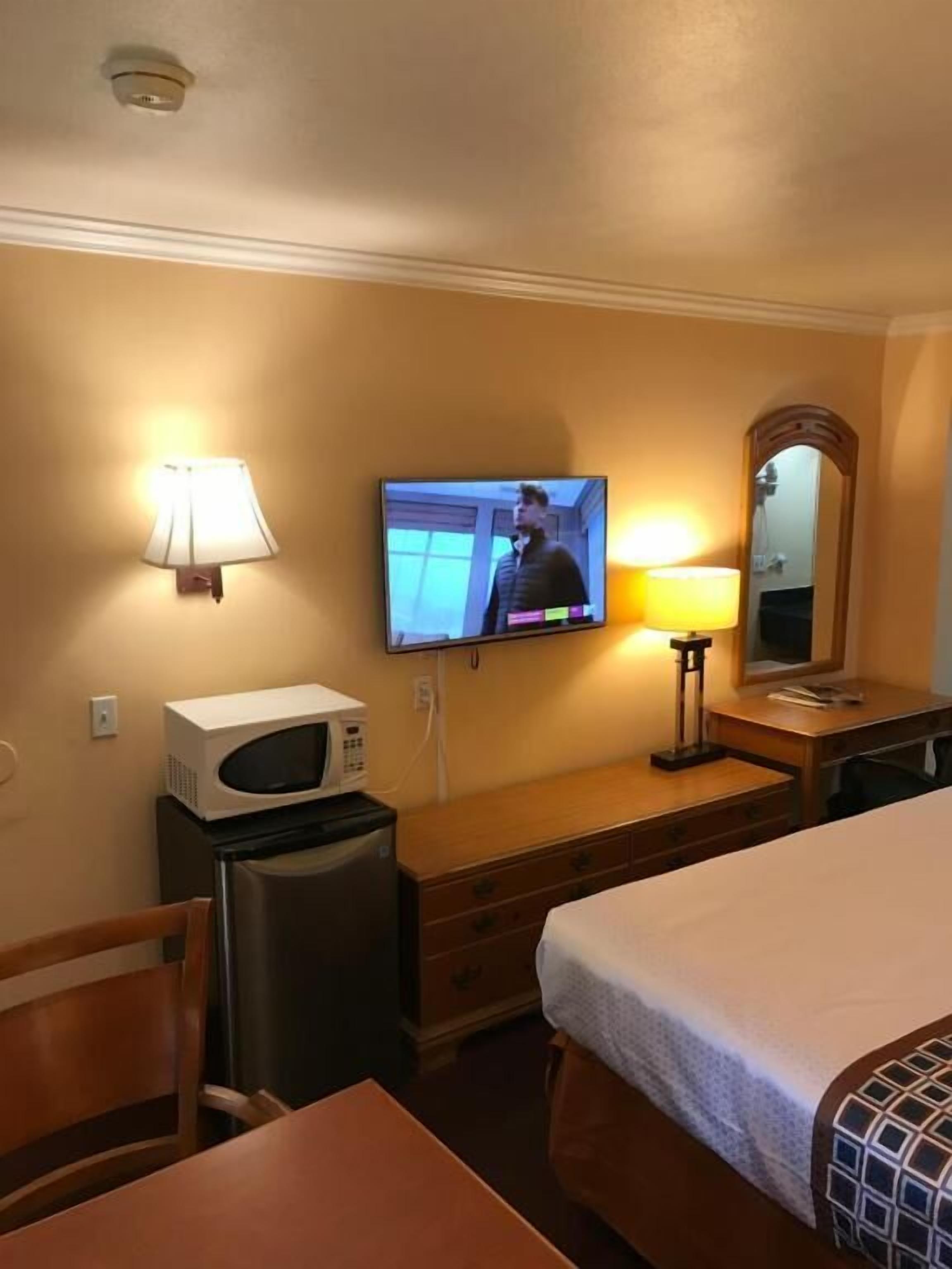 A hotel room with a bed, a desk, a microwave, a television, and a lamp.