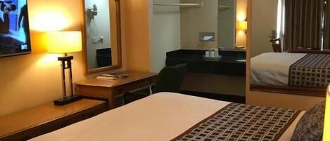 Una habitación de hotel con cama, escritorio, silla, televisor y espejo.