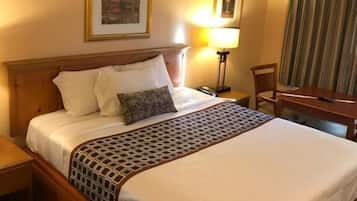 A hotel room with a large bed, a nightstand, a desk, and a chair.
