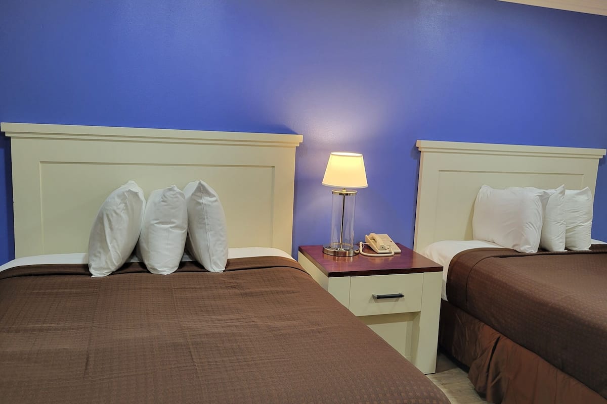 Ein Hotelzimmer mit zwei Betten, jeweils mit weißen Kissen und brauner Bettwäsche. Dazwischen befindet sich ein Nachttisch mit Lampe und Telefon.