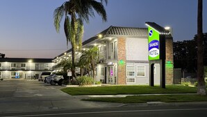 A motel with multiple rooms, a parking lot, and a palm tree. - Sands Motel (Riverside)