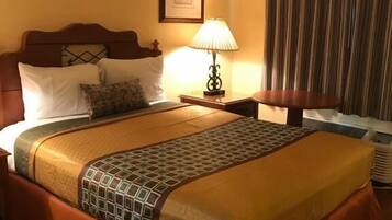 A hotel room with a large bed, a bedside table with a lamp, a framed picture on the wall, and a window with curtains.