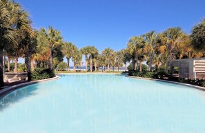 Una piscina grande y cristalina rodeada de palmeras y un edificio a un lado.