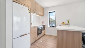 Une cuisine moderne avec des meubles en bois, un réfrigérateur blanc, un four encastré et une fenêtre donnant sur une vue sur la montagne.