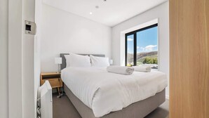 Une chambre d’hôtel moderne avec un grand lit, une table de chevet, une fenêtre donnant sur les montagnes et un thermostat fixé au mur.