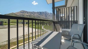 Un balcon avec une table et des chaises, d’où l’on peut admirer une route et des montagnes.