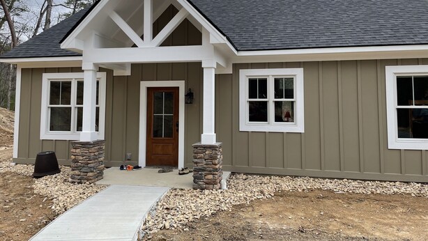 A modern house with a gabled roof, a front porch with stone pillars, and a front door with a glass panel. - Serenity, Waterfront Mountain Retreat (Eagle Rock)