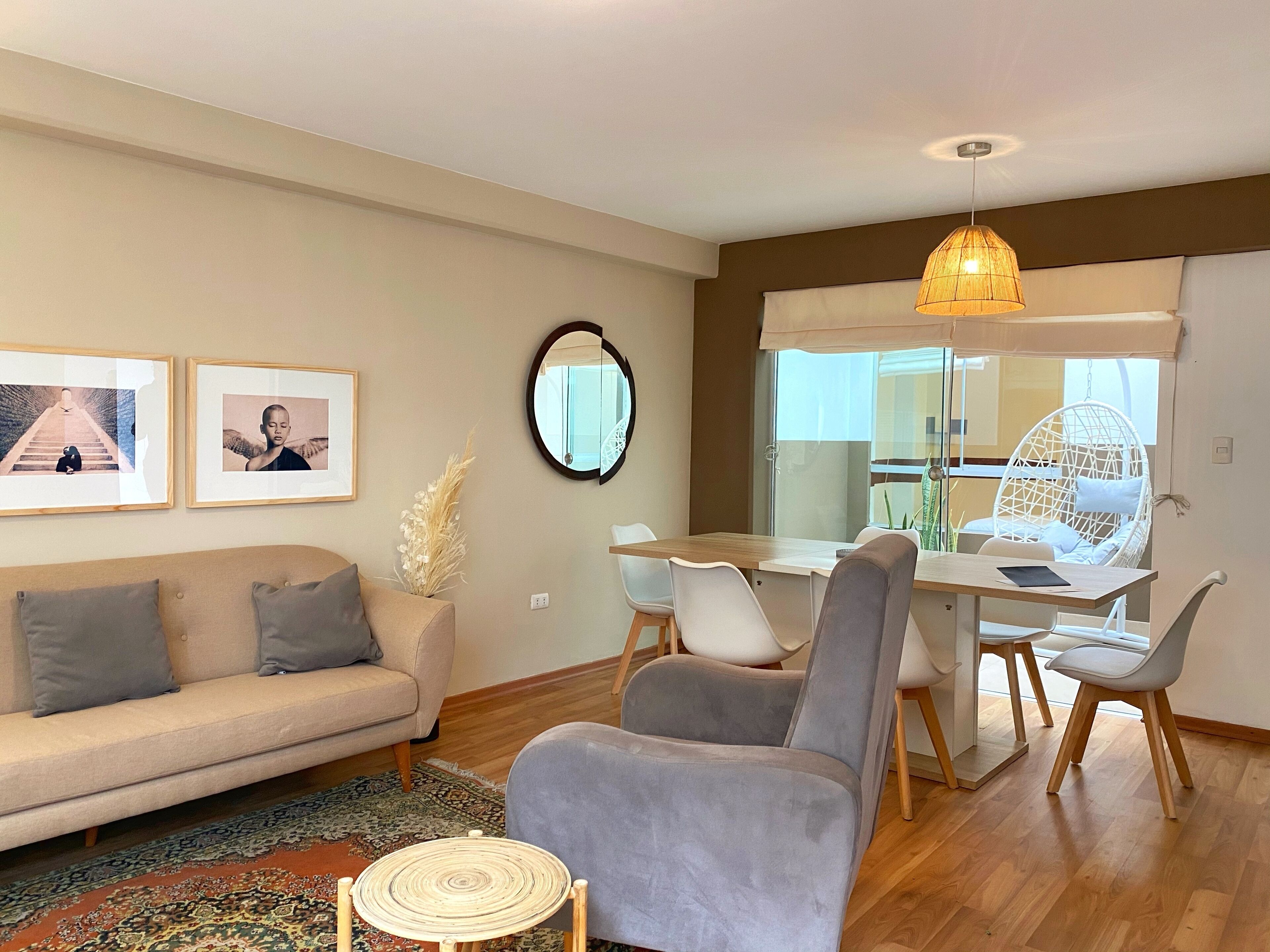A modern living room with a sofa, a dining table with chairs, a hanging chair, and a small round table.