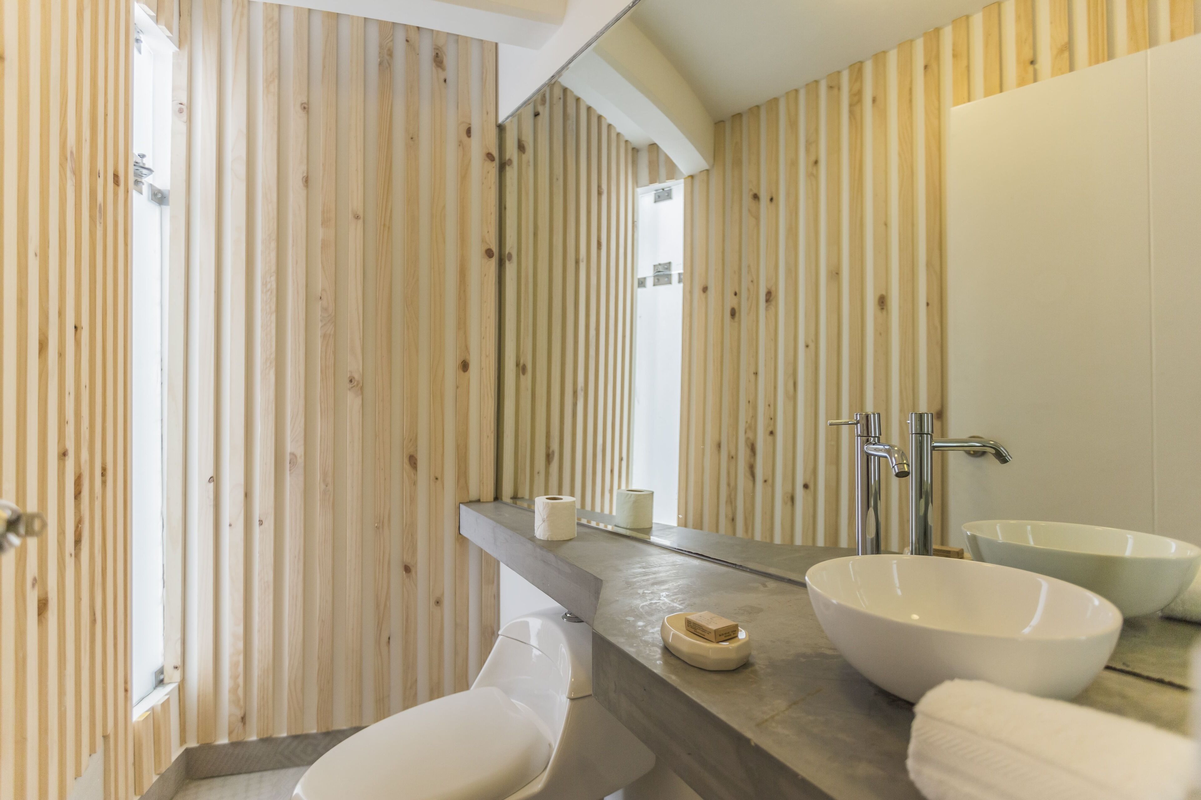 Une salle de bain avec des murs recouverts de panneaux en bois, un grand miroir, deux lavabos et des toilettes.