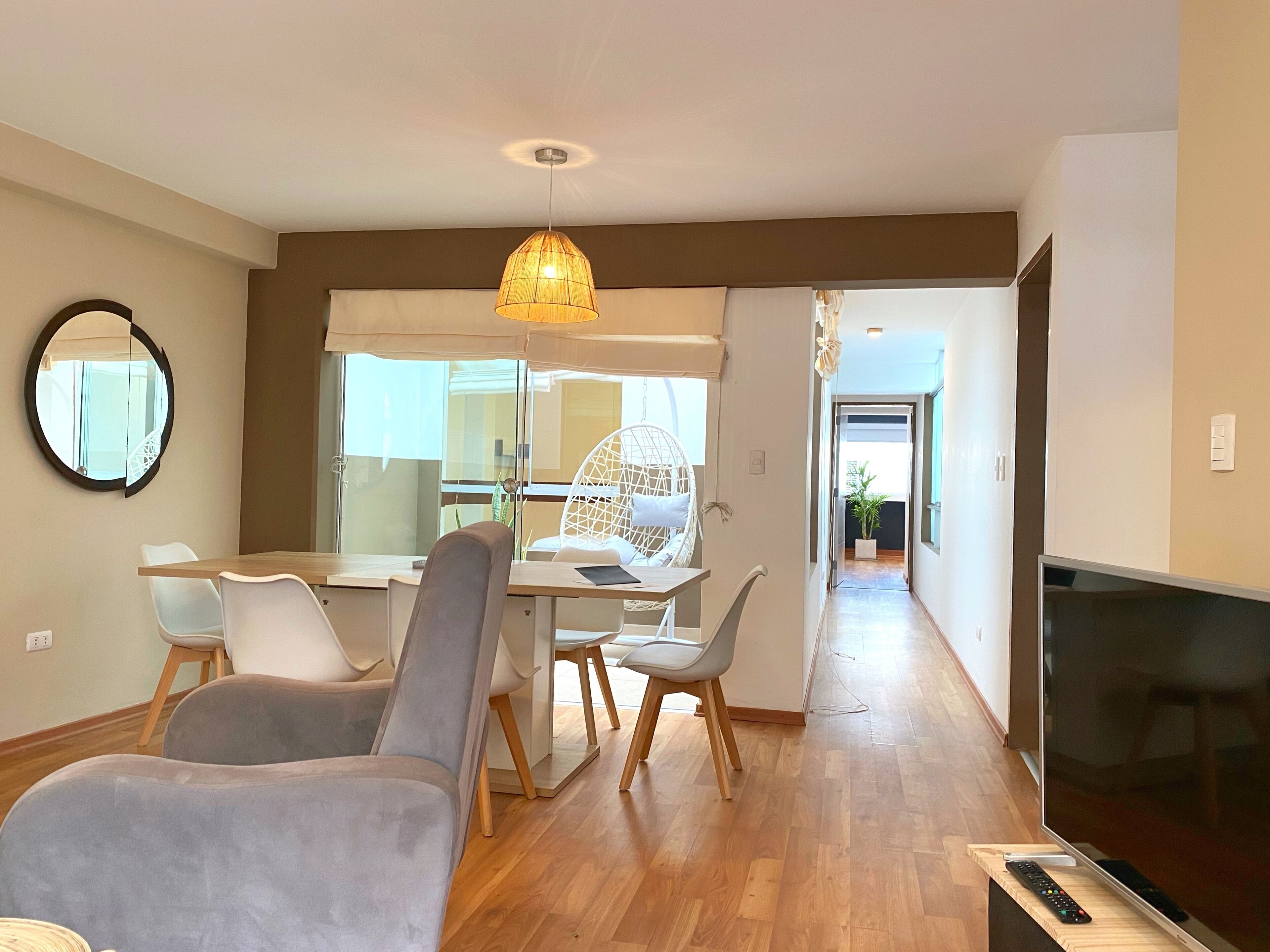 A modern living room with a dining area, a TV, and a large window.