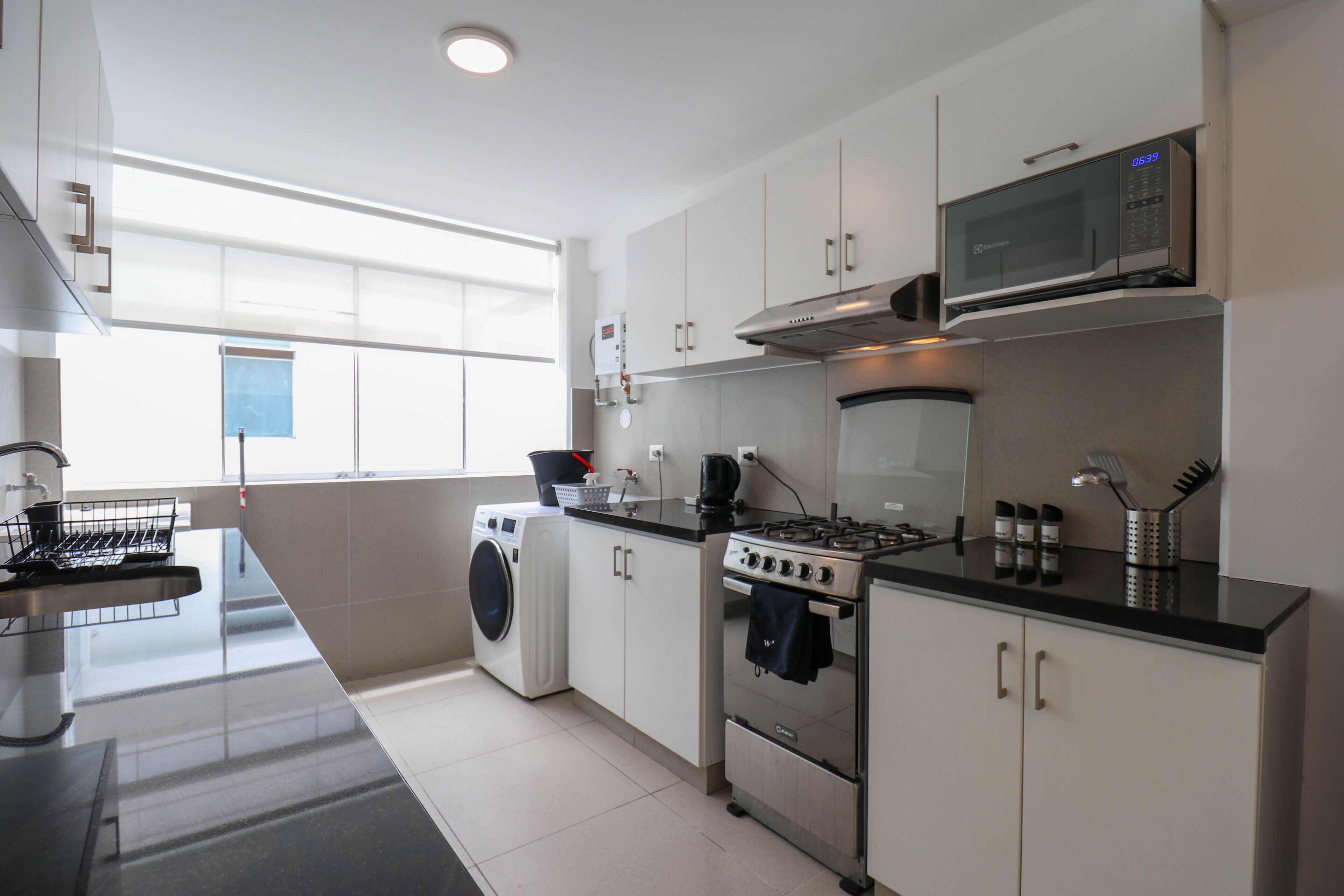Una cocina moderna con electrodomésticos de acero inoxidable, un microondas, una estufa y una lavadora.