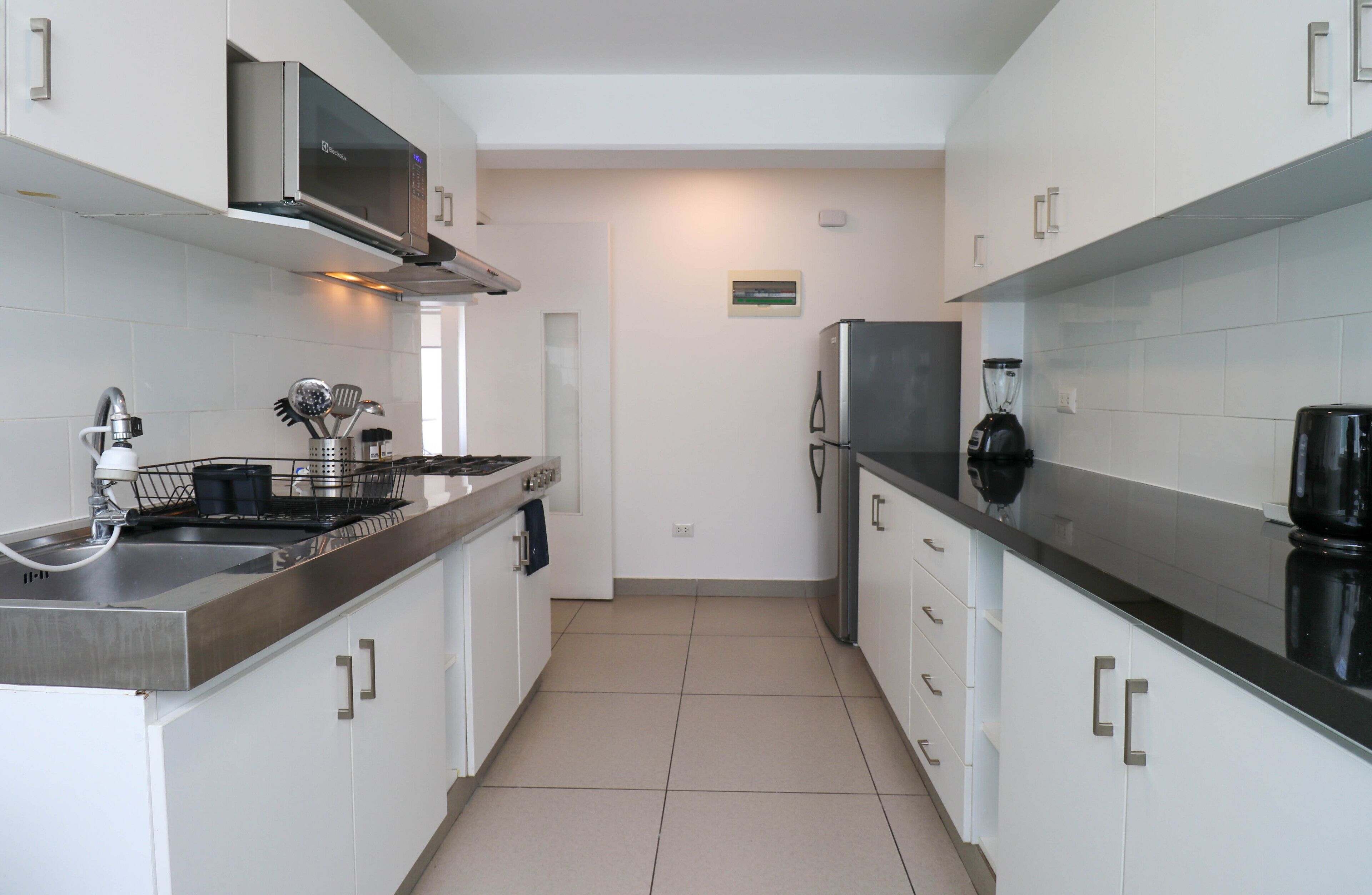 A modern kitchen with stainless steel appliances, white cabinets, and a tiled floor.