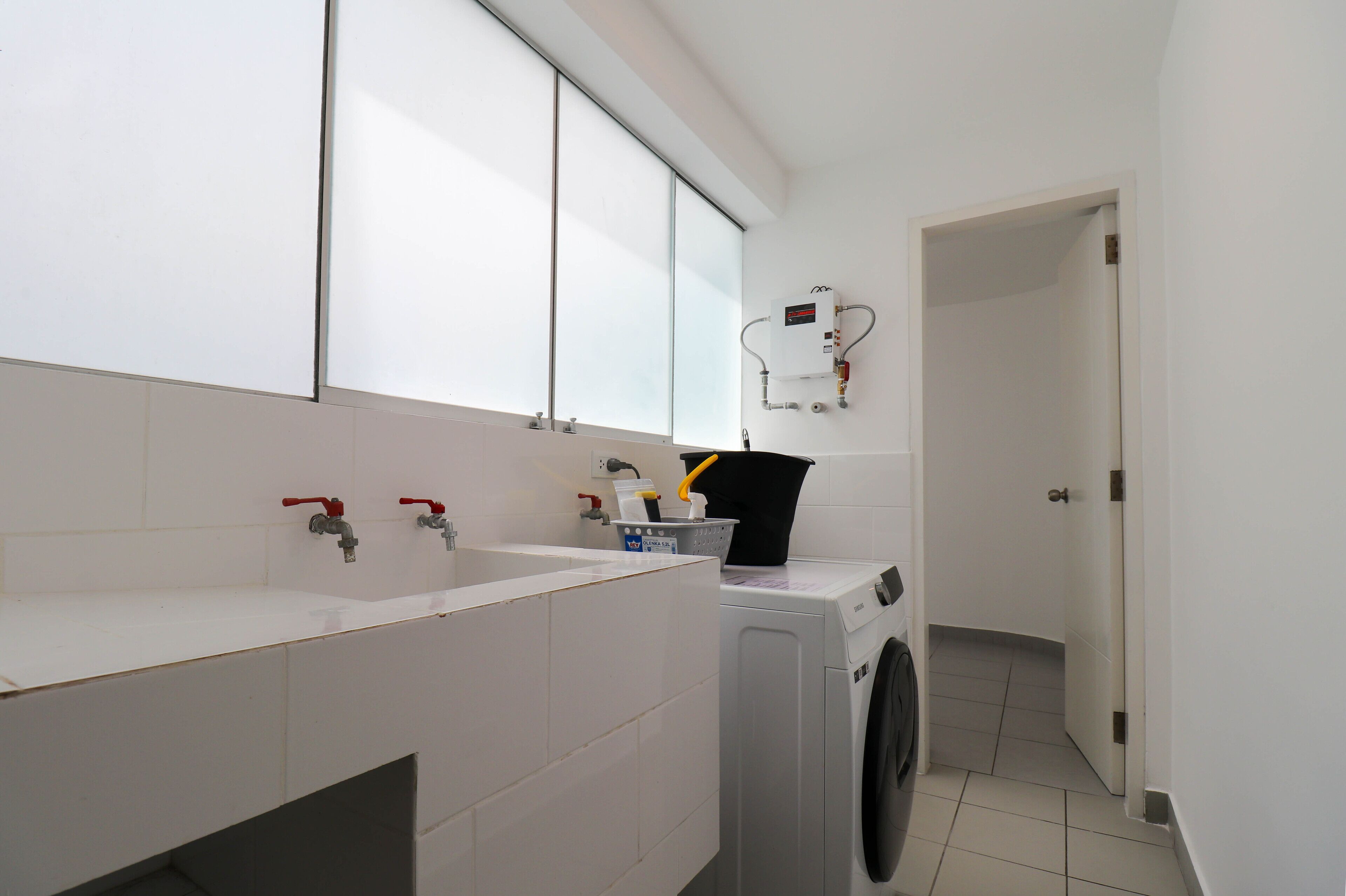 A modern bathroom with a large window, a washing machine, and a sink with two faucets.