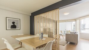 Un espacio de oficina moderno con una mesa de madera, sillas blancas, un sofá gris y una obra enmarcadas en la pared.