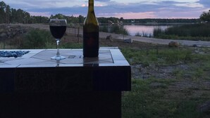 Une table avec une bouteille de vin et un verre, donnant sur un paysage naturel avec une étendue d’eau et des arbres.