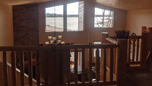 Une pièce spacieuse avec de grandes fenêtres donnant sur un plan d’eau, un mur d’accent en pierre et une balustrade en bois.