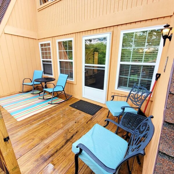A covered patio area with wooden flooring, blue chairs, and a striped rug.