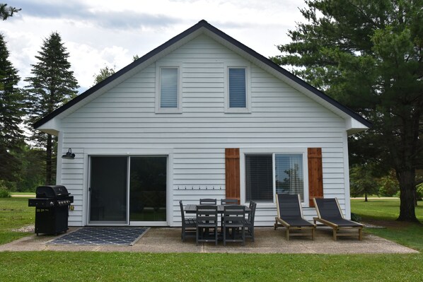 A two-story house with a patio area featuring a grill, a table with chairs, and two lounge chairs.