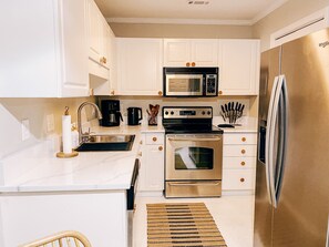 Uma cozinha moderna com armários brancos, eletrodomésticos de aço inoxidável, incluindo uma geladeira, micro-ondas e forno, e uma cadeira de madeira.