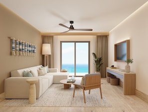 Una sala de estar moderna con sofá, mesa de centro y sillón, ventilador de techo, televisor y vista al océano.