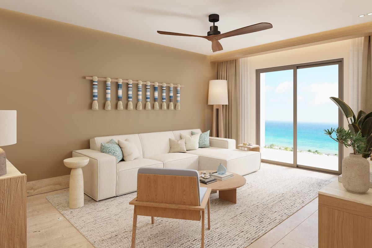 A modern living room with a white sofa, a wooden coffee table, a ceiling fan, and a large window with a view of the ocean.