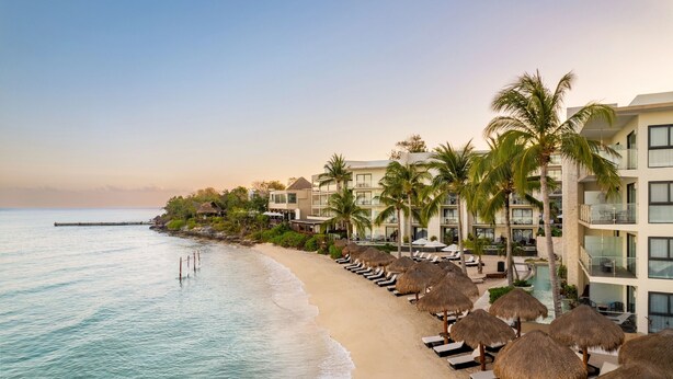 A beachfront hotel with thatched umbrellas, sun loungers, and a pool area. - Dreams Cozumel Cape Resort & Spa - All Inclusive (Cozumel)