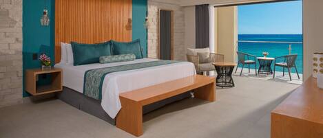 A bedroom with a large bed, a wooden headboard, a bench, a small table, and a view of the ocean.