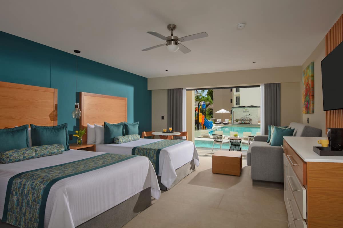 A hotel room with two beds, a desk, a chair, and a view of a pool area.