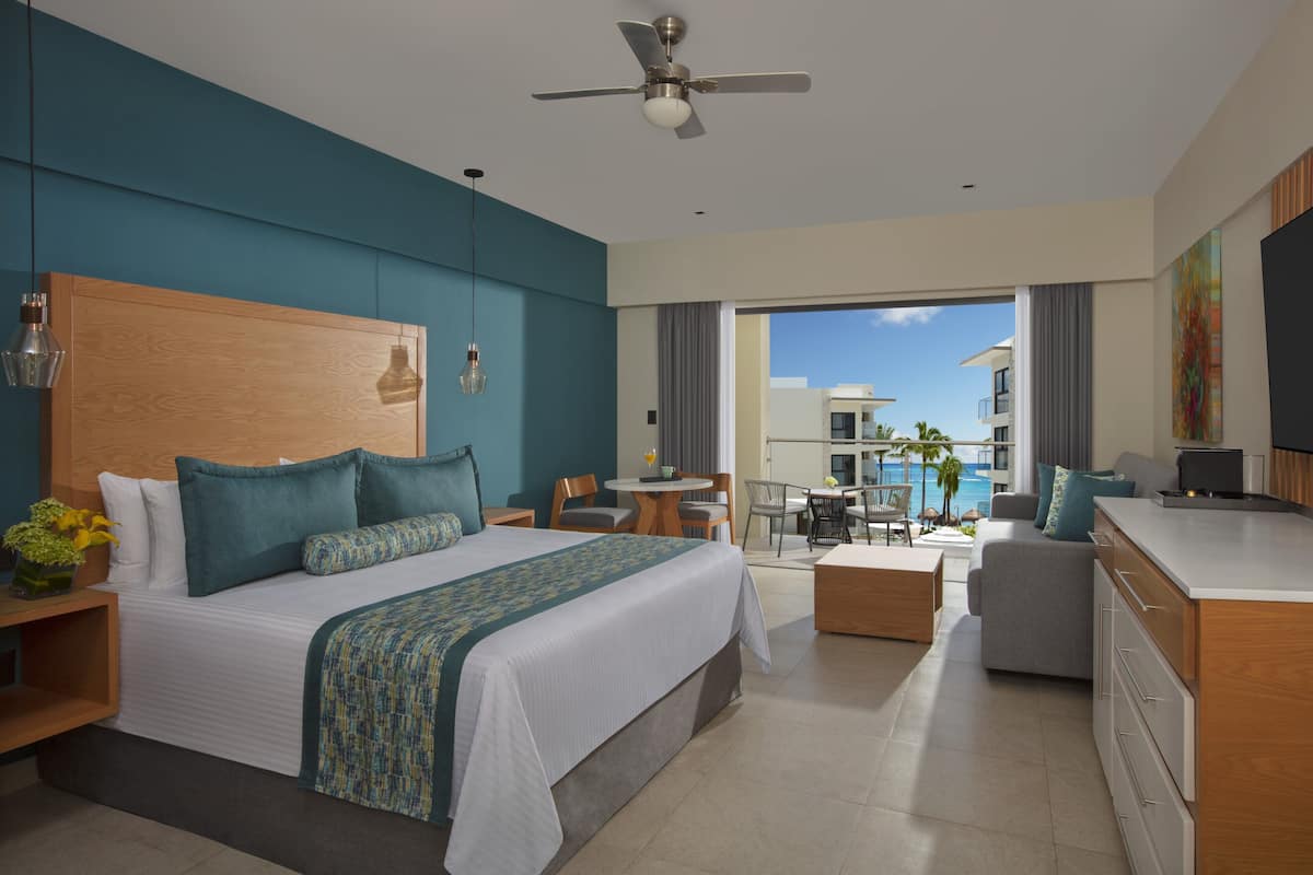 A hotel room with a bed, a desk, a chair, a small table, and a view of the pool.