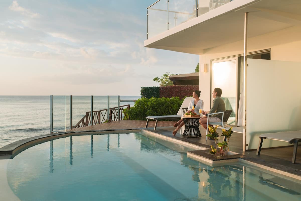 A poolside area with a view of the sea, a glass balustrade, and a seating arrangement.