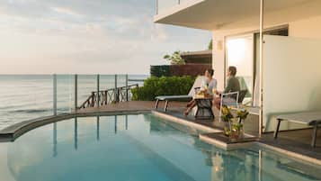 A poolside area with a view of the sea, a glass balustrade, and a seating arrangement.