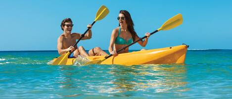 Um casal pratica caiaque em um caiaque amarelo em um mar azul e límpido.