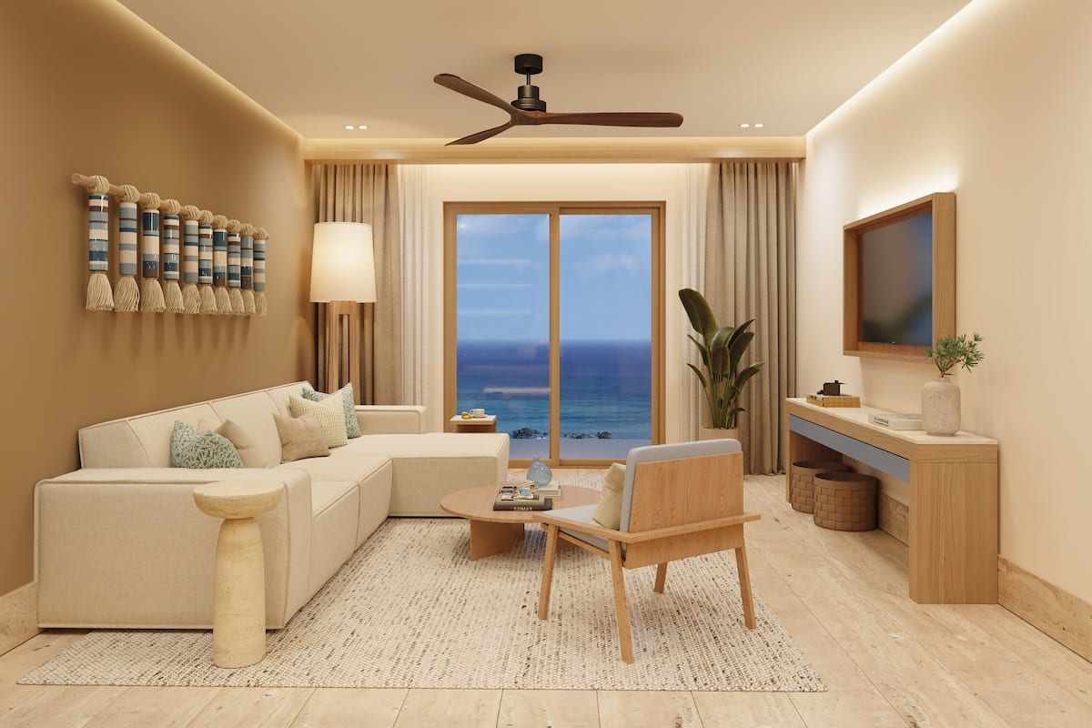 A modern living room with a sofa, coffee table, and a chair, a ceiling fan, a large window with a view of the ocean, and a TV mounted on the wall.