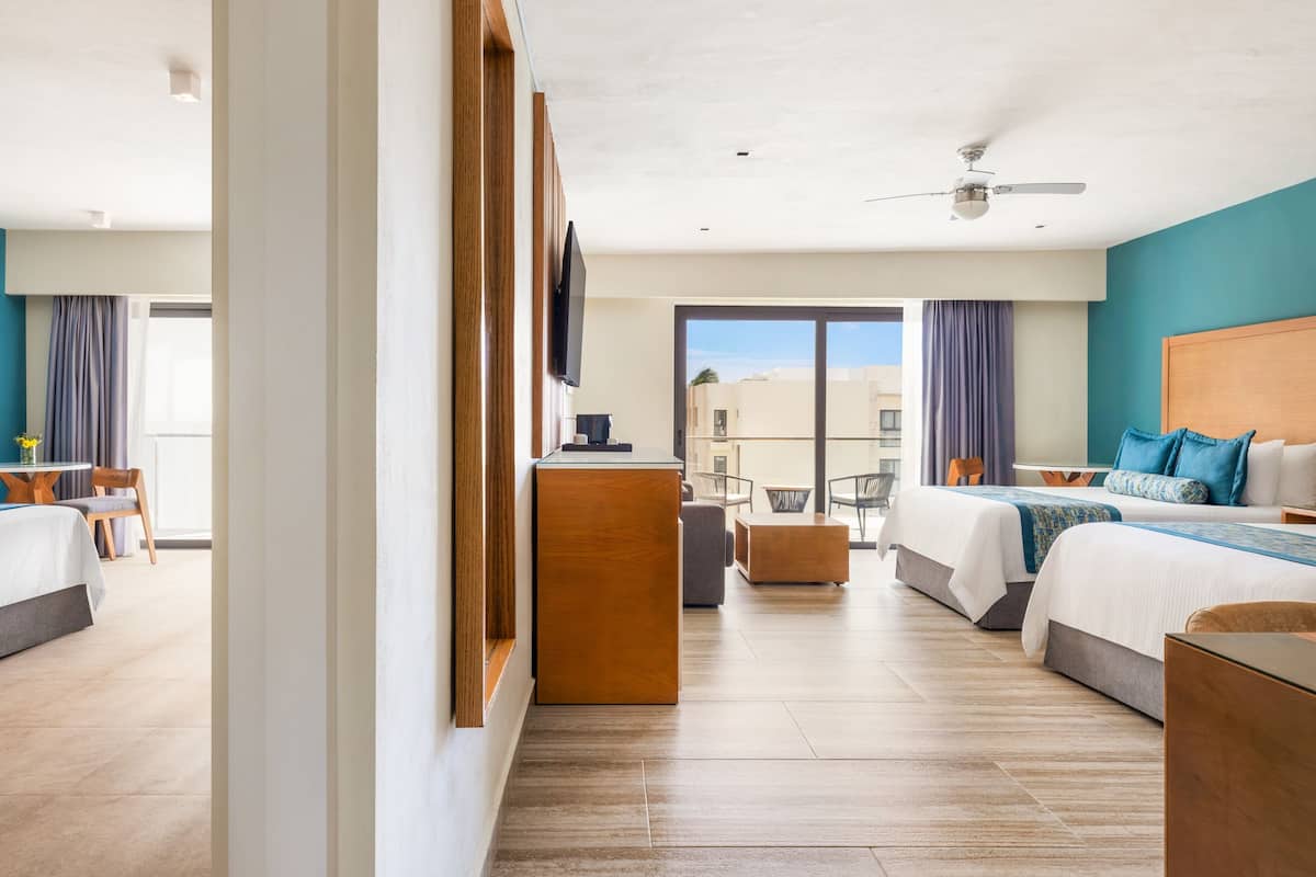 A hotel room with two beds, a desk, a TV, and a balcony with a view.