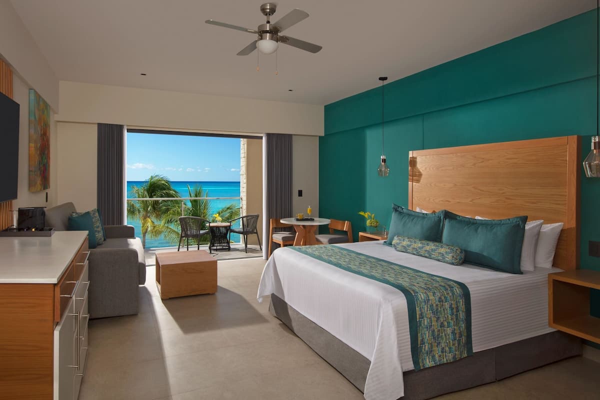 A modern hotel room with a large bed, a desk, and a balcony with a view of the ocean.