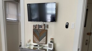 Una camera da letto con un letto, una cassettiera, un televisore fissato al muro e una porta che dà su un'altra stanza.