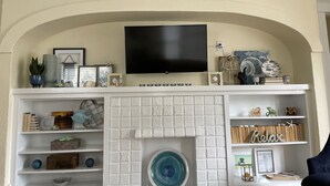Un soggiorno con camino, scaffali decorati e una TV a parete, con un cartello che dice "Love the Beach".