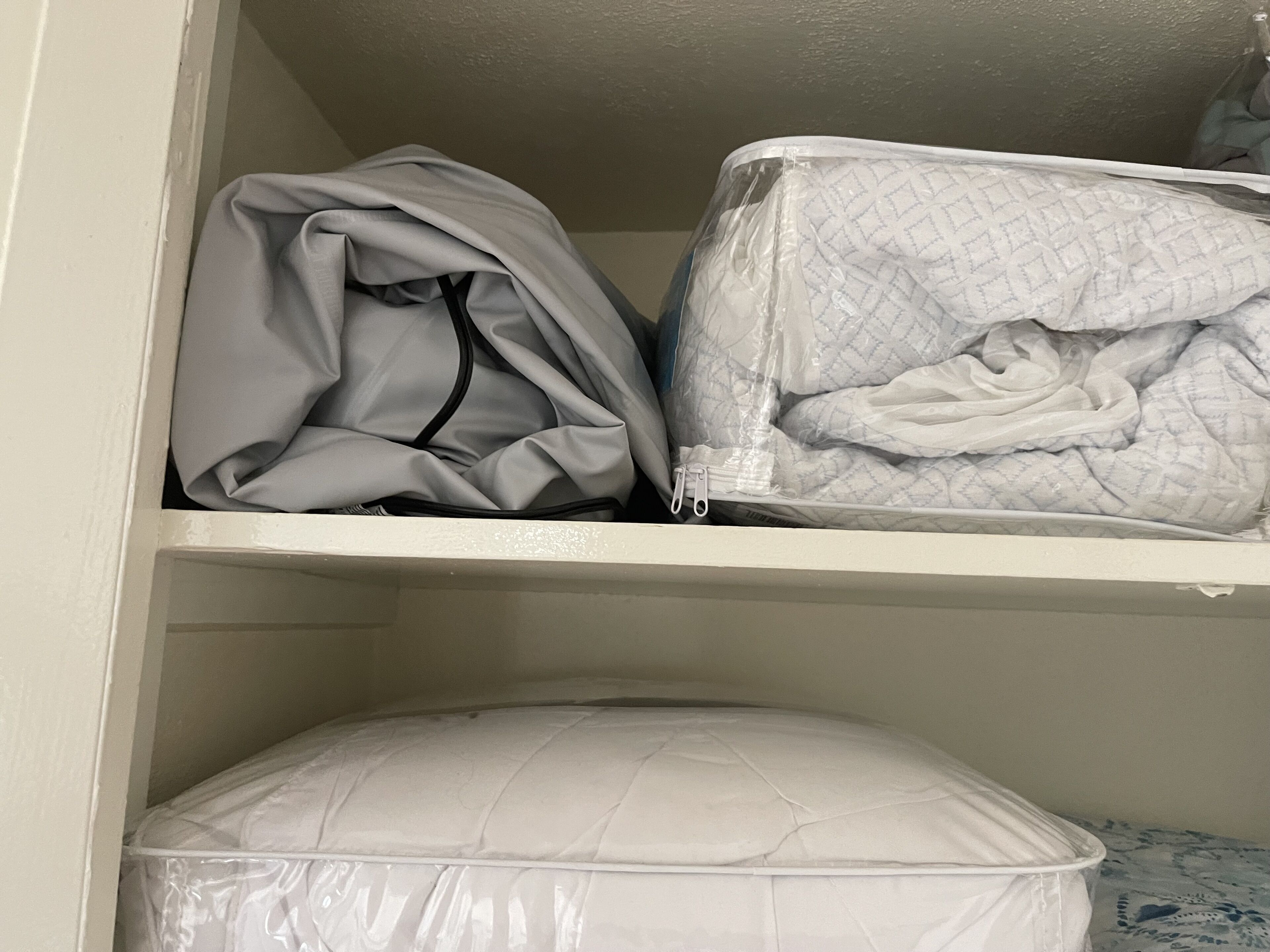 Un armario con una chaqueta doblada y una colcha acolchada en la repisa superior, y una almohada en la repisa inferior.