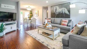 Una sala de estar moderna con un sofá gris, una mesa de centro, un televisor y un comedor con sillas y una mesa.