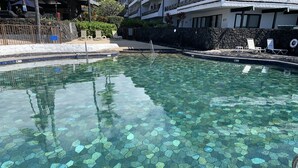 Una piscina cristalina con mosaicos hexagonales, rodeada de sillones de descanso y un muro de piedra.