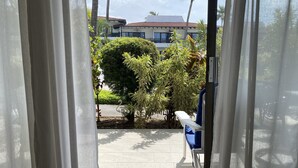 Vista a través de una puerta con felpudo decorado con un diseño de pez, que da a un área pavimentada con un banco y una palmera.