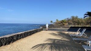 Una playa con un muro de piedra, una persona caminando y sillas de playa a lo largo de la orilla.