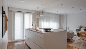 Eine moderne Küche mit Kochinsel, Pendelleuchten und einem Essbereich mit Tisch und Stühlen.